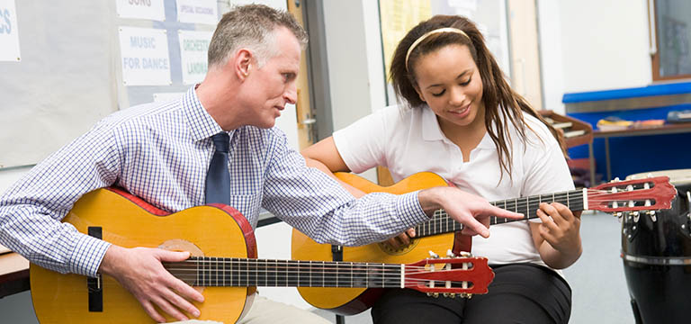Guitar teaching helping student with hand position on the guitar.