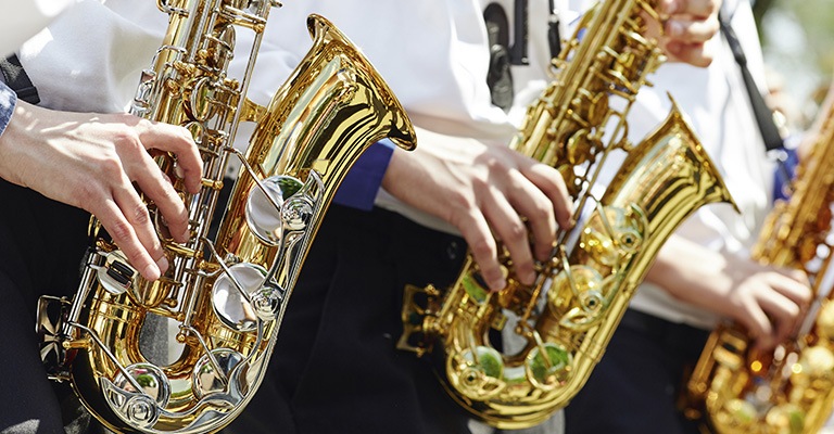 A group of young musicians in the youth brass band play on the golden saxophones at a concert in the city park.