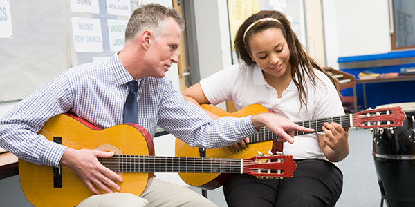 Schoolgirl and teacher playing acoustic guitar in music class