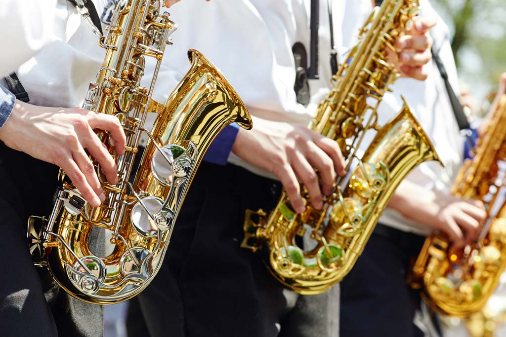 A group of young musicians in the youth brass band play on the golden saxophones at a concert in the city park.